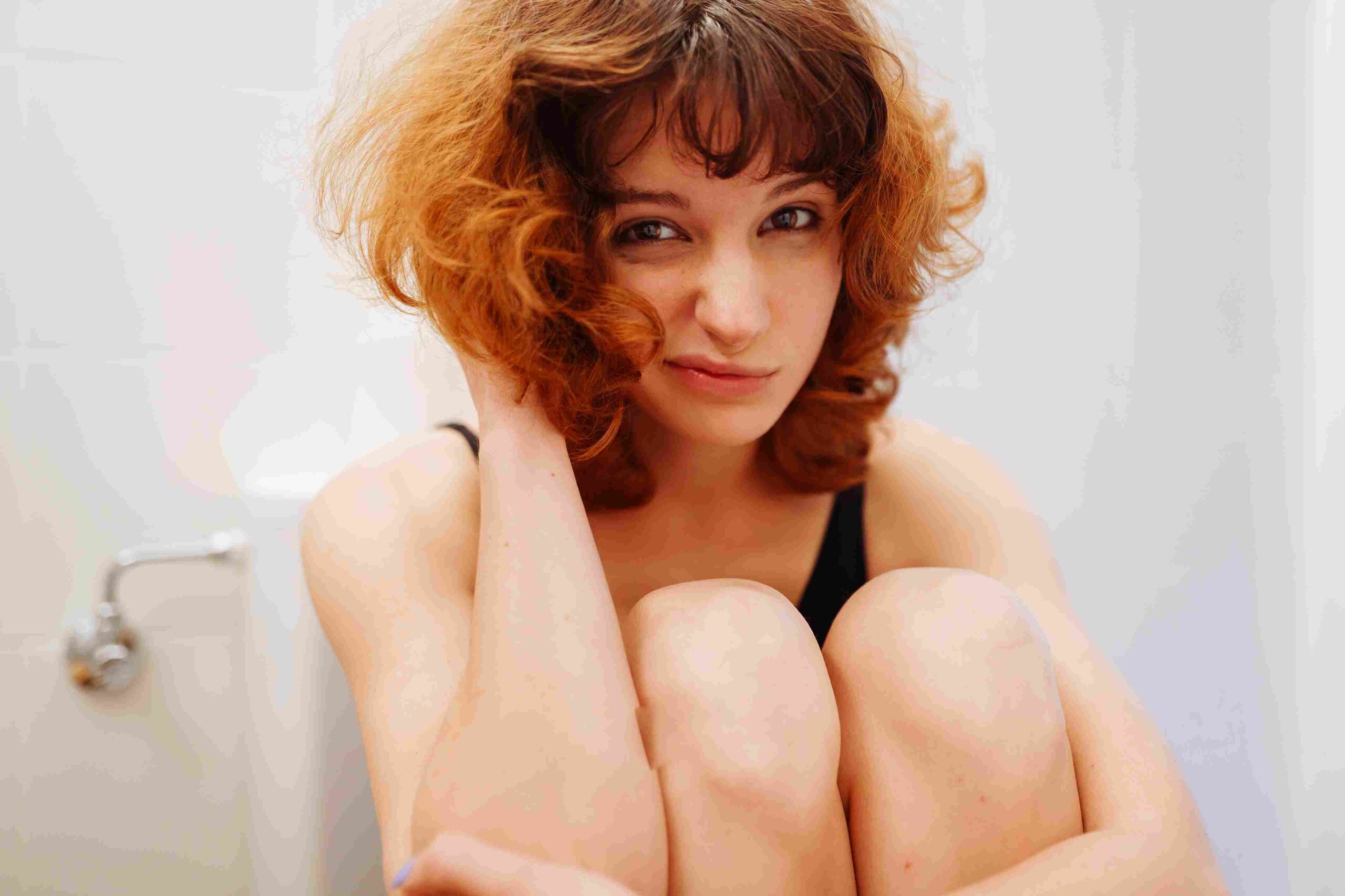 Žena sedi u kupatilu i drži kolena